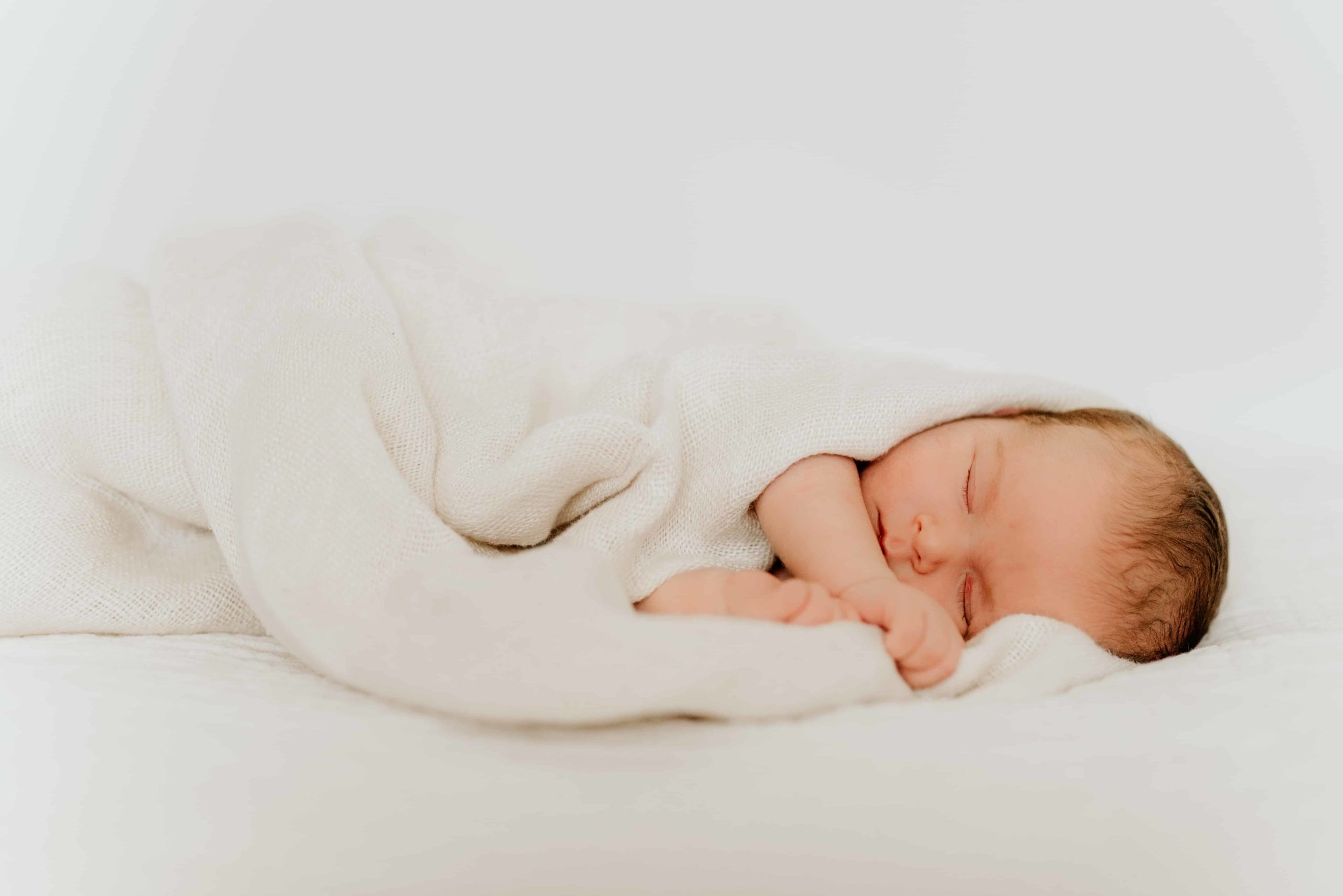 En nyfødt jentebaby ligger på siden og sover under naturlig nyfødtfotografering.